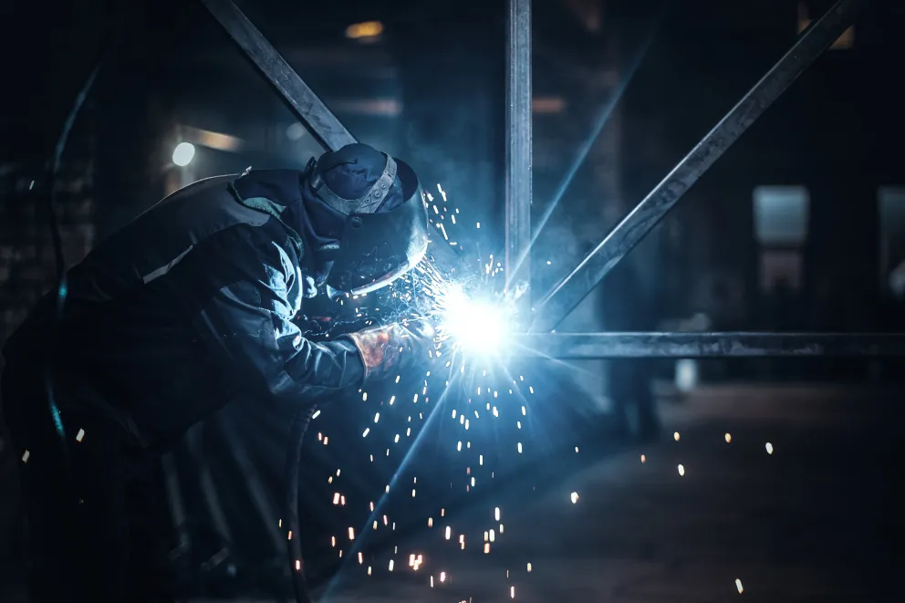 Homem com equipamento de solda realizando a solda e fa&iacute;scas saindo